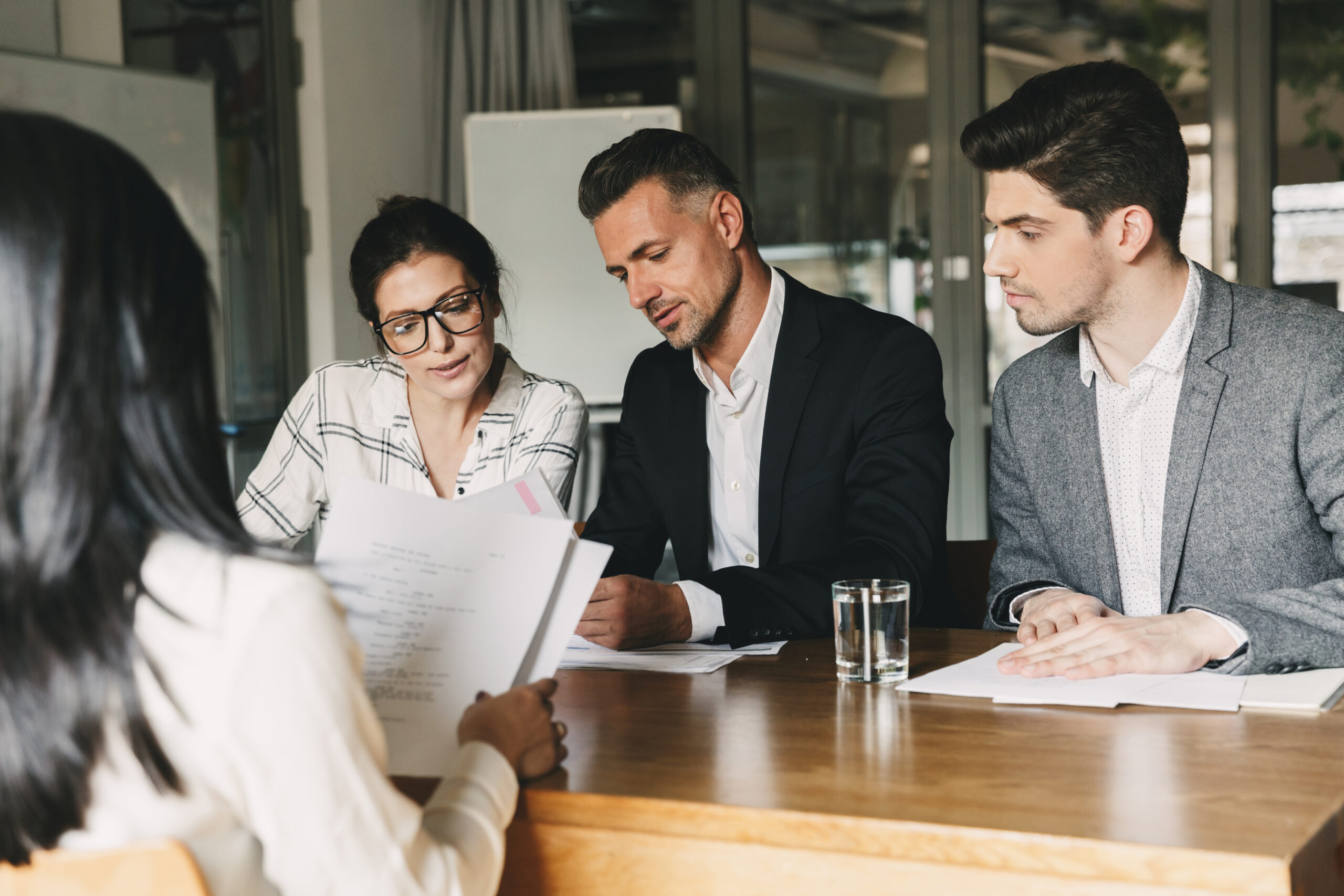 Drei Personen sitzen an einem Tisch und prüfen gemeinsam Dokumente in einem Bürogespräch